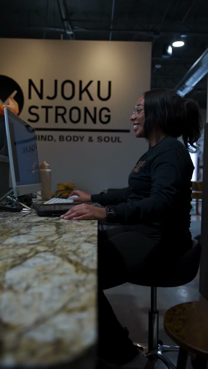 The front desk at the Njoku Strong studio in Westlake: a staff member at a marble-topped counter beneath the Njoku Strong — Mind, Body and Soul wall mark.