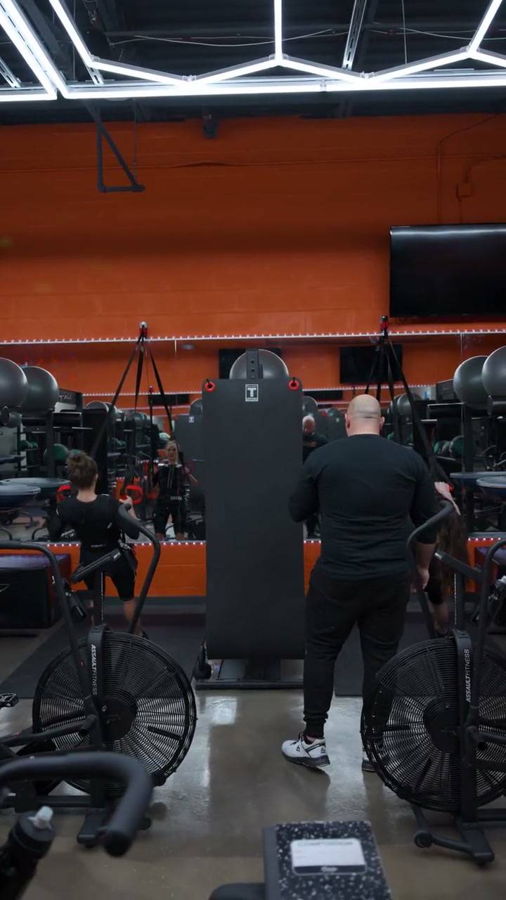 The current Njoku Strong training floor in Westlake: members mid-session among air bikes and suspension rigs in front of the orange feature wall.