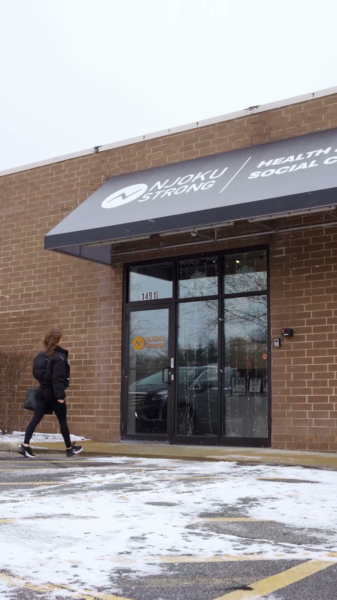 The Njoku Strong storefront at 1491 Columbia Road in Westlake: brick walls under a black awning reading Njoku Strong — Health & Social Club, a member walking toward the glass doors across a snow-streaked lot.