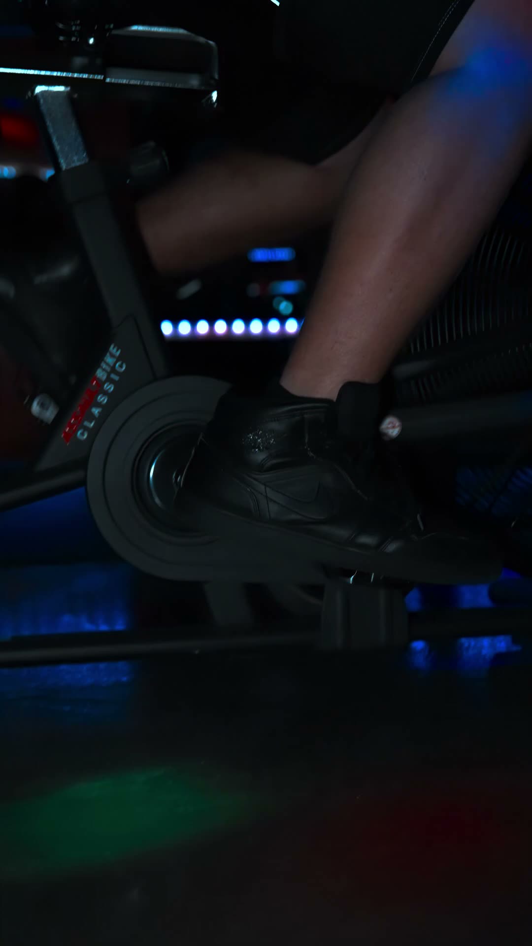 A member driving a studio bike under blue and green LED light on the Njoku Strong training floor in Westlake.